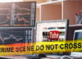 Cinta policial en frente de escritorio de trader con pantalla de inicio de youtube en pantalla. Composición por CriptoNoticias. zfijr / piqsels.com; geralt / pixabay.com; mstandret / elements.envato.com.
