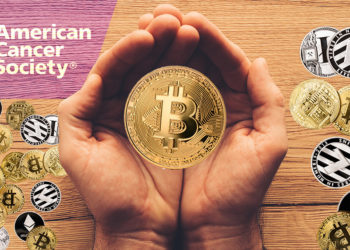 Manos sostienen moneda de Bitcoin con criptomonedas y logo de la Sociedad Americana contra el Cancer sobre mesa de madera. Composición por CriptoNoticias. LightFieldStudios / elements.envato.com; ff-photo / elements.envato.com; American Cancer Society / cancer.org; stevanovicigor / elements.envato.com.